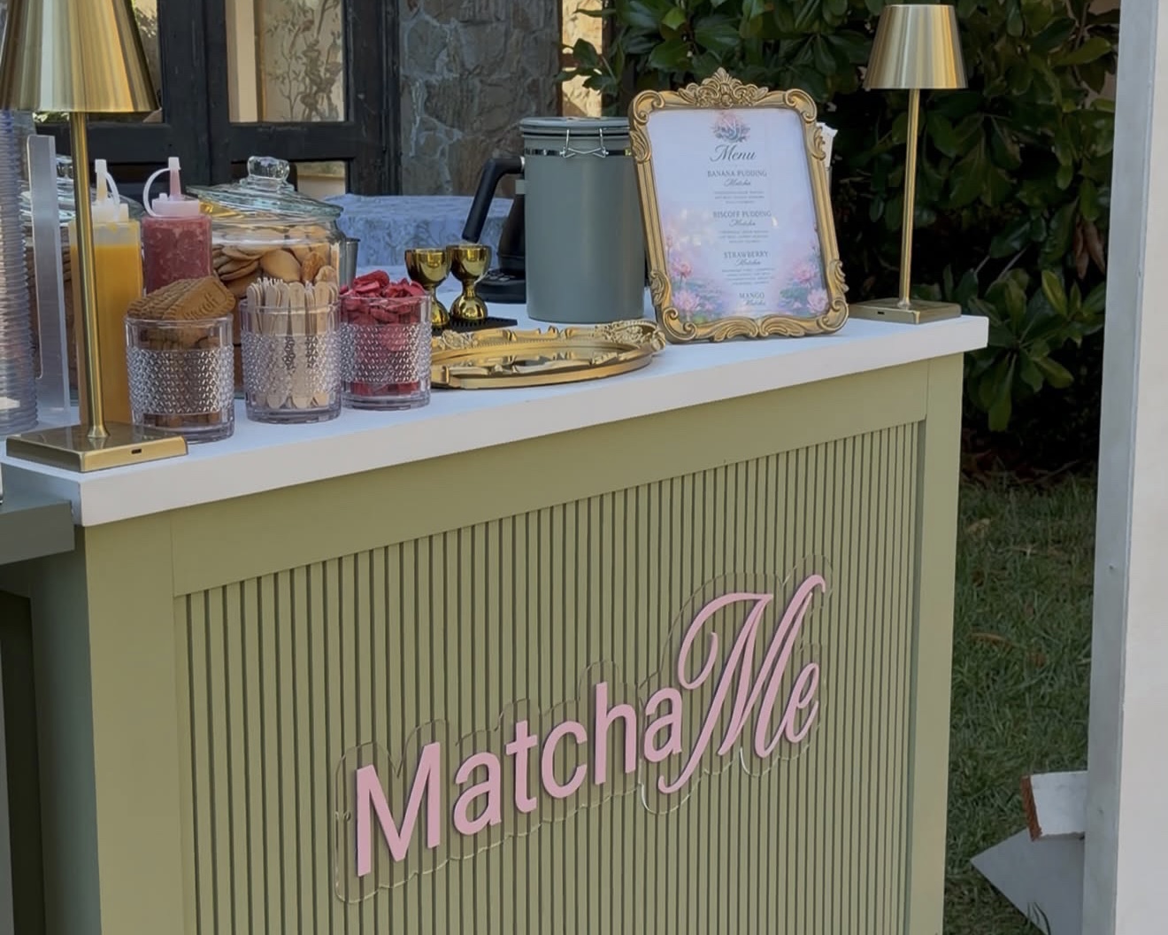 The Matcha Me cart at an event with a gold-framed menu and styled glassware